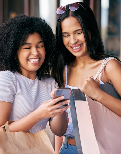 Amigos de compras e mulheres com telefone no shopping desfrutando de tempo de qualidade de liberdade e fim de semana juntos Sacos de compras smartphone e meninas rindo de meme online mídia social e internet