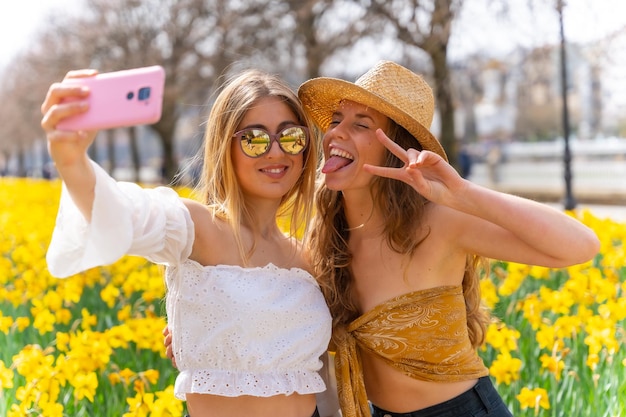 Amigos de férias na cidade com chapéus de palha ao lado de algumas lindas flores amarelas sorrindo muito e aproveitando a primavera tirando uma selfie