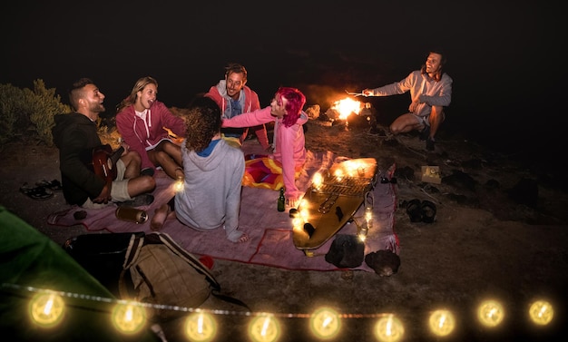 Amigos de jovens hippies se divertindo juntos na festa à noite na praia com luz de corda