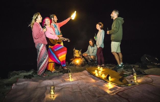 Amigos de jovens hipster se divertindo juntos na festa de acampamento na praia com luz de fogueira noturna