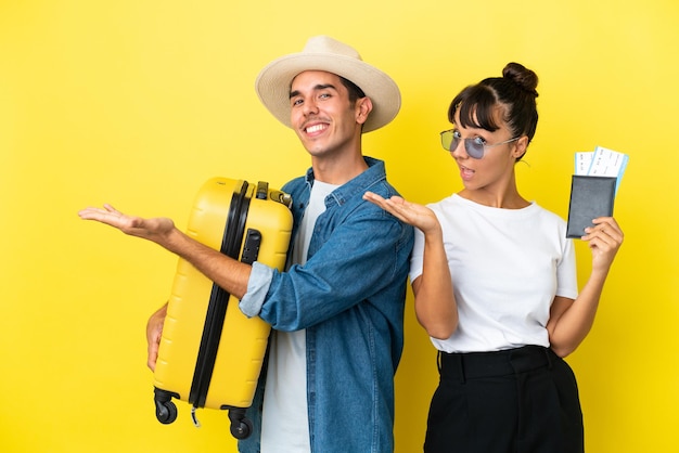 Amigos de jovens viajantes segurando uma mala e passaporte isolados em fundo amarelo, estendendo as mãos para o lado para convidar para vir