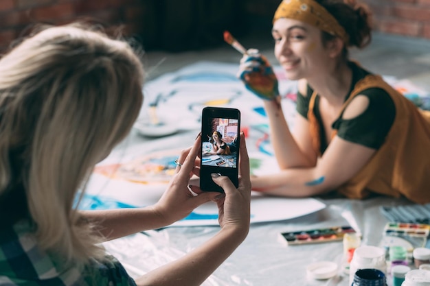 Amigos de lazer Senhora tirando foto de jovem artista posando no chão com tinta e pincel sorrindo