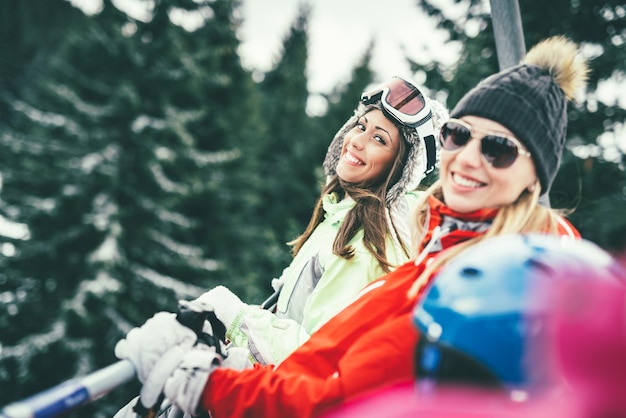 Amigos de mulher jovem e bonita desfrutando de férias de inverno. Eles dirigindo no teleférico e olhando para a câmera com um sorriso.