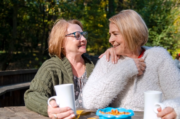 Amigos de mulheres idosas desfrutar de bebida quente, sentado no terraço. idosos bebendo chá. cintura retrato