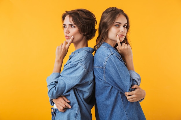 Amigos de mulheres jovens pensativos isolados sobre a parede amarela.