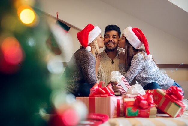 Amigos de natal adoráveis brincalhões felizes com chapéus de papai noel e suéteres desfrutando de casa para as férias.