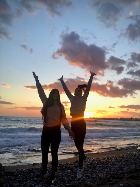 Amigos de pé na praia contra o céu durante o pôr do sol