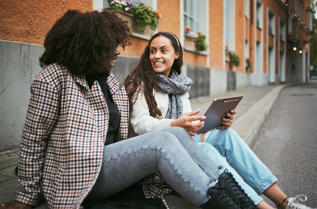 Amigos de rua e mulheres conversando sobre tablet e mídia social para conexão, conversa e união ao ar livre Jovens do sexo feminino e dispositivo para leitura on-line da cidade e meninas na estrada e discussão