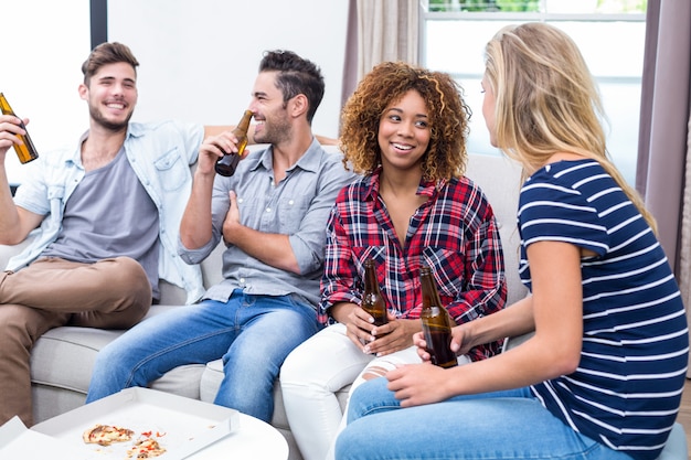 Amigos, desfrutando de cerveja enquanto está sentado no sofá em casa