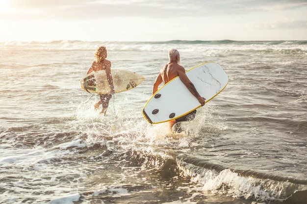 Amigos de diferentes edades corriendo en la playa al atardecer para el entrenamiento de surf