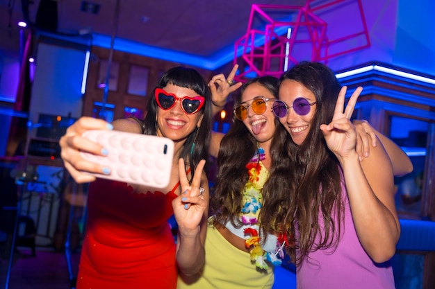 Foto amigos en una discoteca tomándose un selfie con el teléfono en una fiesta nocturna en vacaciones de verano en un pub