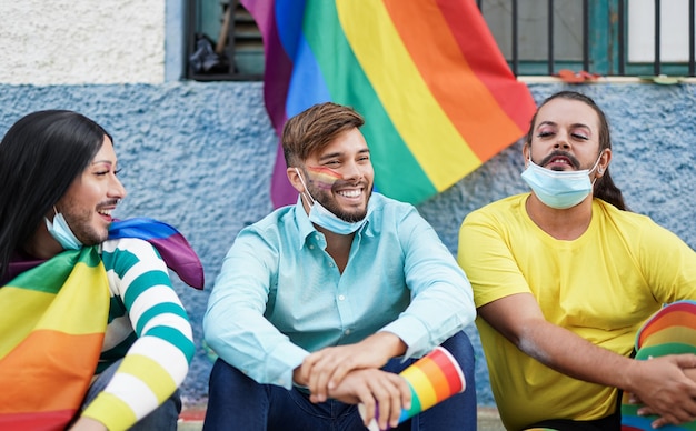 Amigos disfrutando del desfile lgbt: hombres homosexuales y transgénero con mascarilla quirúrgica debajo de la barbilla por brote de coronavirus