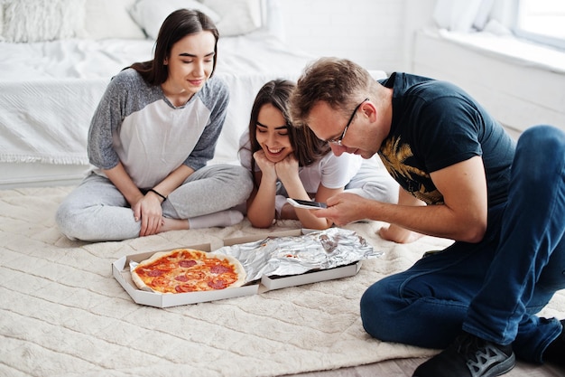 Amigos disfrutando y pasando tiempo juntos Niñas gemelas con caja de pizza Hombre mirando en el teléfono móvil