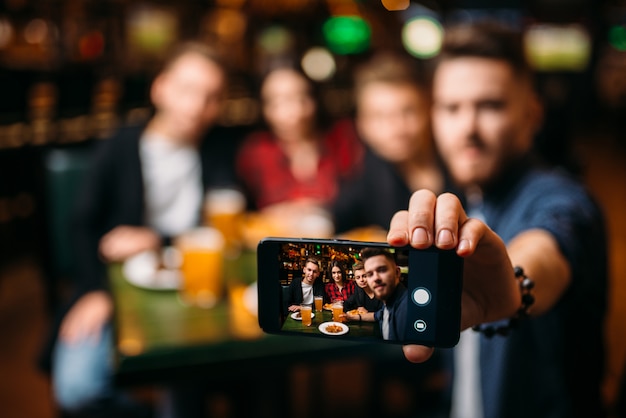 Amigos divertidos fazem selfie no telefone em um bar esportivo