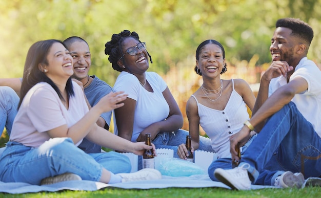 Amigos divertidos y picnic al aire libre en el parque se ríen de la comedia con diversión juntos y cerveza con comida en la naturaleza Felicidad cómica y diversidad en la amistad hombres y mujeres uniéndose y riendo