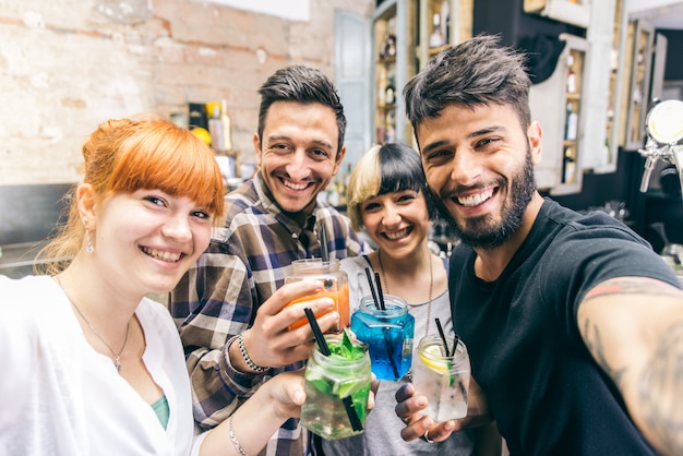 Amigos divirtiéndose en un bar con cócteles y tomando selfies