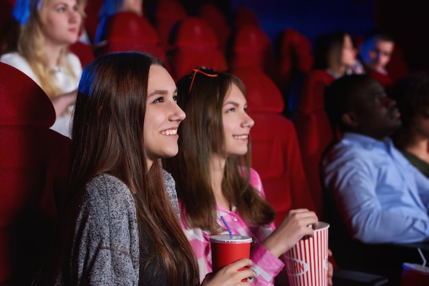 Amigos do sexo feminino alegres novos atrativos que apreciam assistindo a um filme no conceito das emoções da positividade da felicidade do entretenimento da recreação do cinema junto.