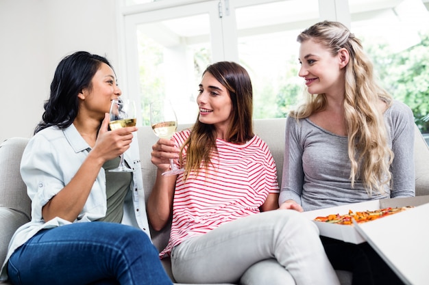 Amigos do sexo feminino com pizza, bebendo vinho em casa