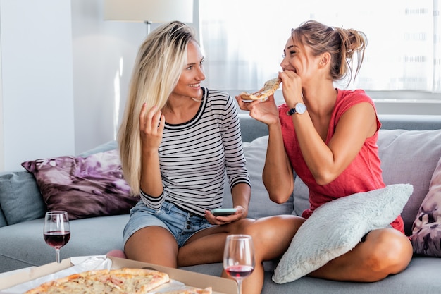 Amigos do sexo feminino comendo pizza com vinho no sofá em casa