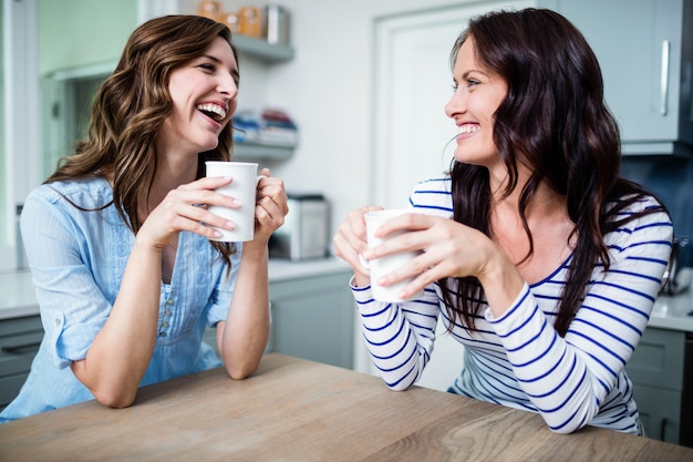 Amigos do sexo feminino felizes segurando canecas de café enquanto discutia na mesa