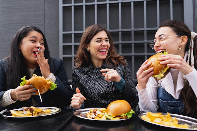 Amigos do sexo feminino passando algum tempo juntos, sorrindo e conversando, sentados à mesa, comendo comida.