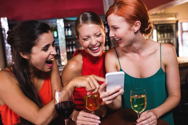 Amigos do sexo feminino usando telefone celular enquanto desfruta de vinho