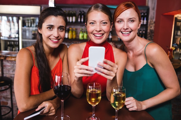 Amigos do sexo feminino usando telefone celular enquanto desfruta de vinho