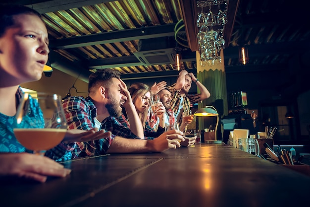 Amigos do sexo masculino e feminino chateados, assistindo a jogos de  esporte ou jogo de futebol e bebendo cerveja em um bar ou pub.