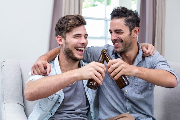 Amigos do sexo masculino jovens alegres brindando cerveja em casa