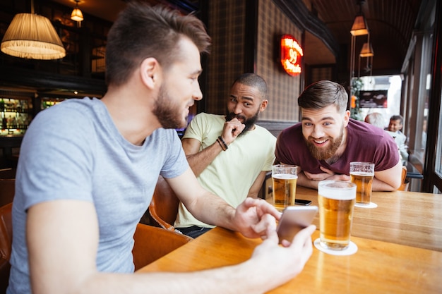 Amigos do sexo masculino rindo olhando para um smartphone em um bar de cerveja