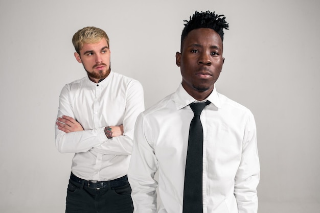 Amigos, dois caras de camisa branca e calça escura posando no estúdio em um fundo branco