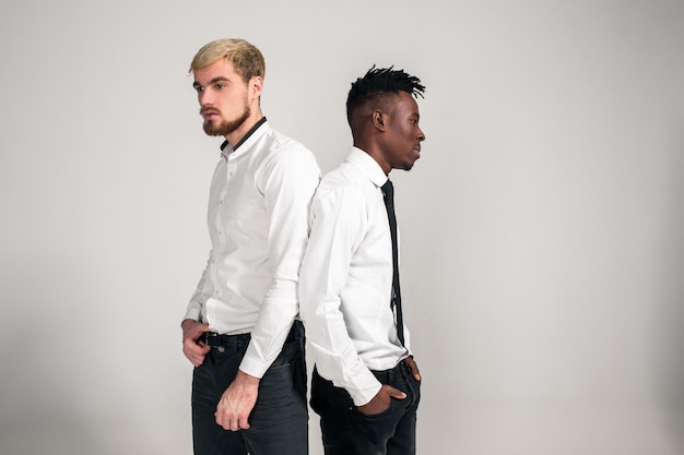 Amigos, dois caras de camisa branca e calça escura posando no estúdio em um fundo branco