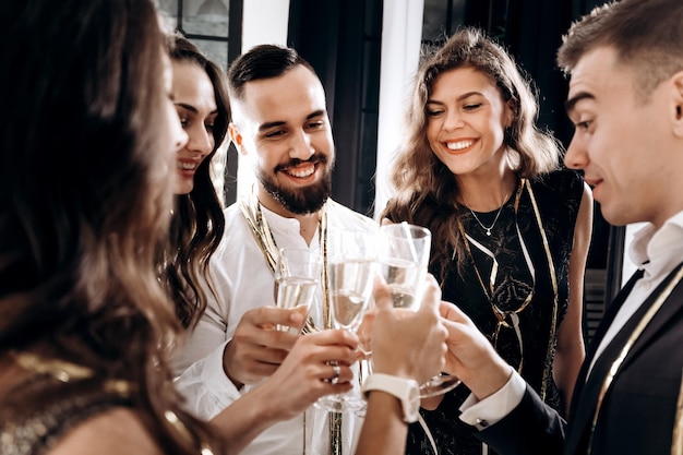 Amigos em roupas elegantes e elegantes sorriem juntos segurando taças de champanhe nas mãos