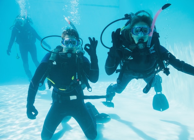 Amigos en el entrenamiento de buceo sumergido en la piscina dos mirando a la cámara