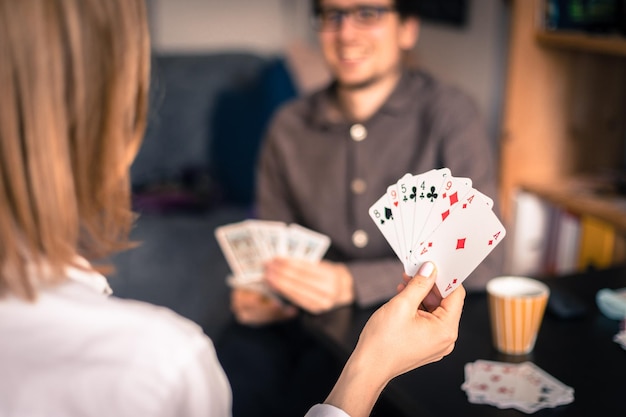 Foto amigos estão jogando cartas juntos em casa mulher está segurando cartas em suas mãos homem no fundo desfocado