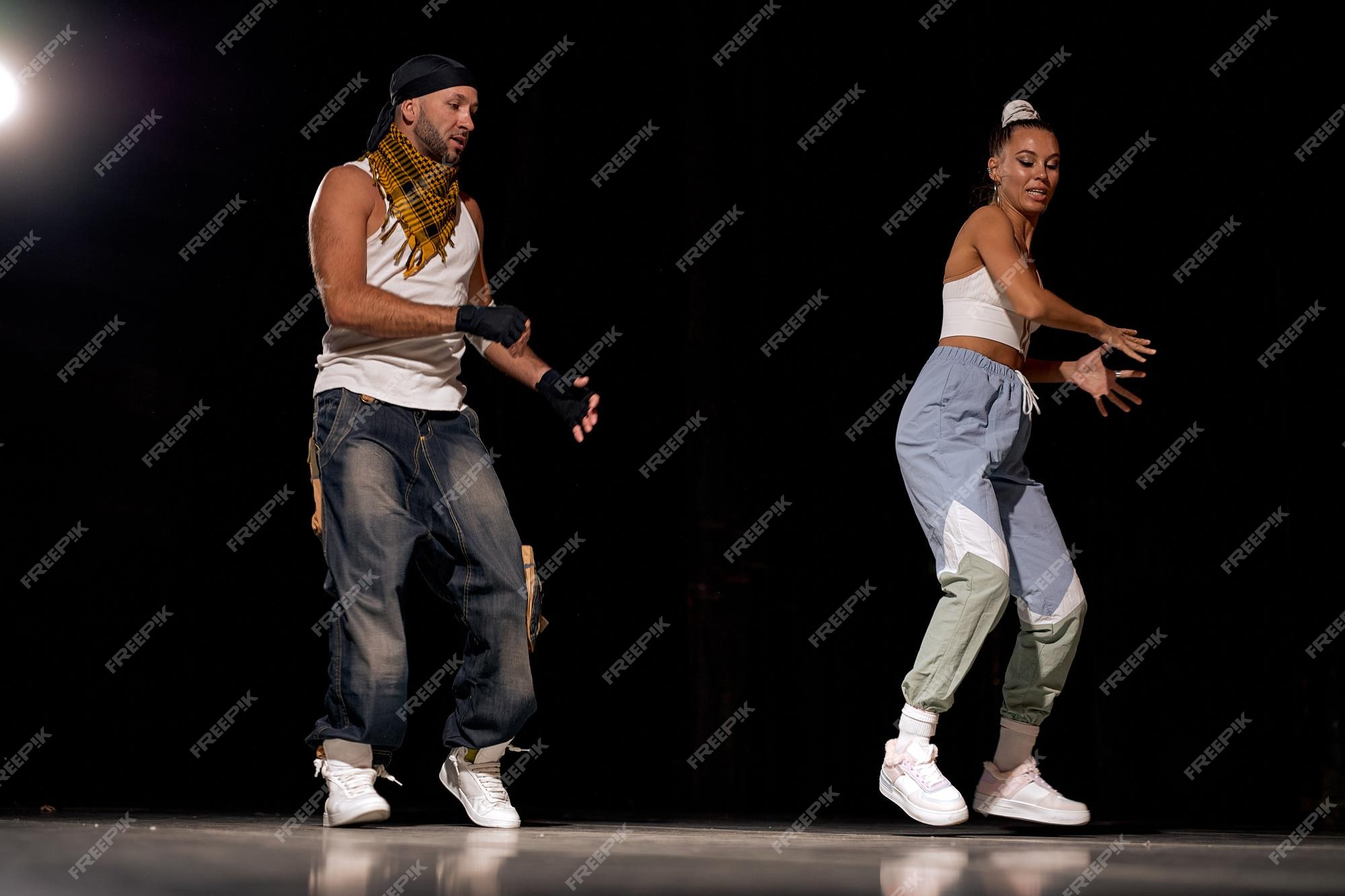 Amigos con estilo hombre y mujer bailando hip-hop en ropa casual sobre fondo negro en el salón baile con luz blanca. cultura juvenil, hip-hop, movimiento, estilo y moda, acción. retrato de