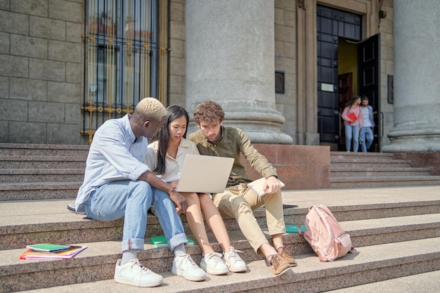 Amigos estudiantes discutiendo noticias de Internet mientras están sentados en los escalones