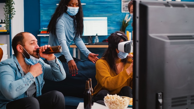 Amigos experimentando realidade virtual jogando videogame usando fone de ouvido vr durante a pandemia social com amigos na sala de estar de casa, respeitando o distanciamento social e usando máscara facial contra a propagação de vírus