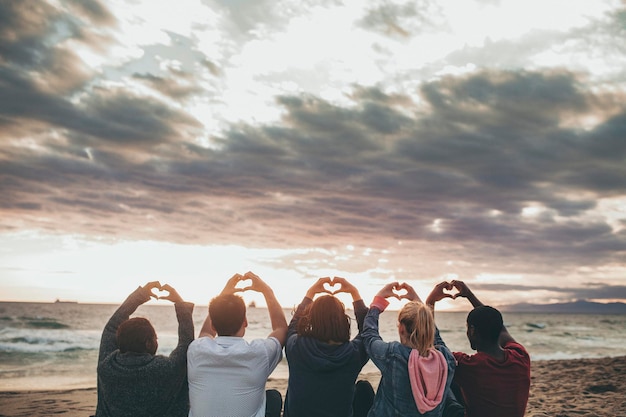 Amigos fazendo amor com mãos de coração na praia