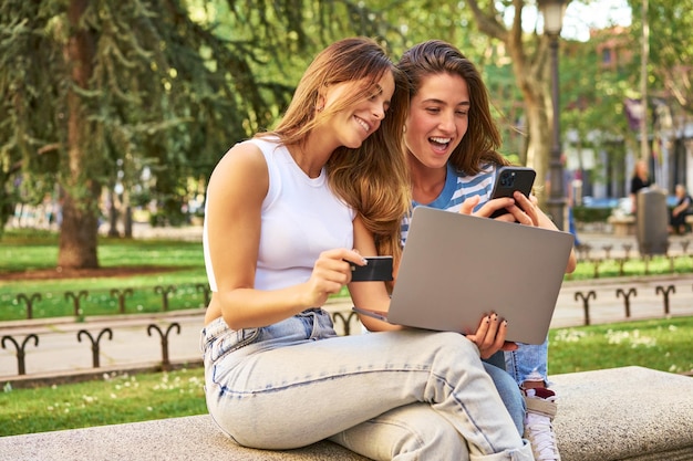 Amigos fazendo compras online com laptop e cartão de crédito no parque
