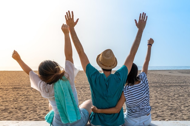 Amigos felices abrazándose unos a otros en la playa con los brazos levantados Alegre abrazando vista posterior