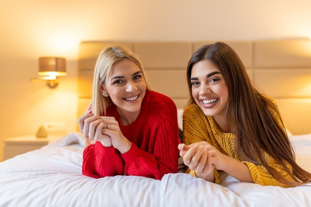 Amigos felices acostados en la cama en casa o en la habitación del hotel sonriendo posando mirando a la cámara el concepto de actividades de ocio de fin de semana perezoso