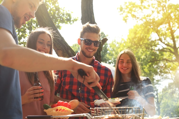 Foto amigos felices asando carne y disfrutando de una fiesta de barbacoa al aire libre.