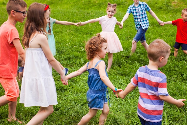 Amigos felices bailando en círculo sobre hierba verde en el día de verano. Infancia feliz