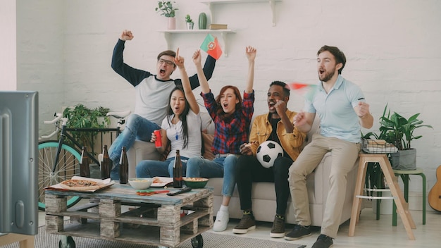 Amigos felices con banderas portuguesas viendo el campeonato deportivo en la televisión juntos en casa y felices por ganar el equipo favorito
