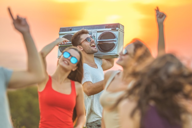 Los amigos felices con un boom box bailando en el fondo del amanecer