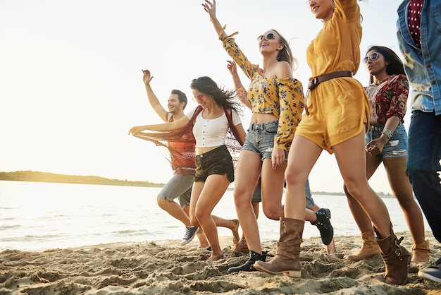 Foto amigos felices corriendo en la playa al atardecer