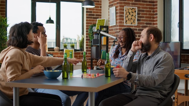 Amigos felices disfrutando de los juegos de mesa de charadas en la reunión de casa, jugando a las adivinanzas con cartas, figuritas y dados. Hombres y mujeres divirtiéndose con actividades tácticas competitivas.