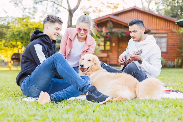 Amigos felices disfrutando de la música del ukelele y al aire libre - Grupo de amigos sentados en el césped con un perro encantador.