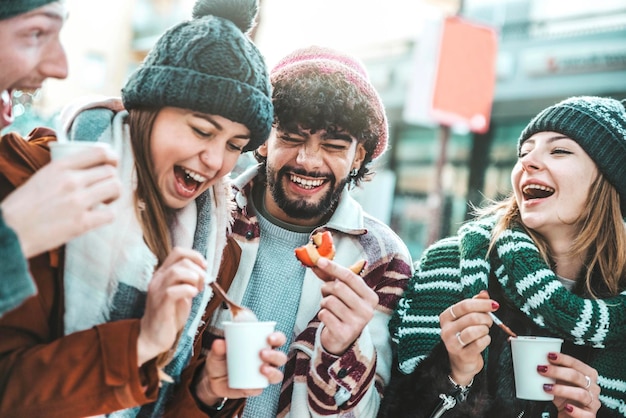 Amigos felices divirtiéndose bebiendo vino caliente y chocolate caliente en el Mercado de Navidad